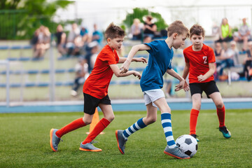 Obraz premium Young boys playing a football game. Training and soccer match between youth school teams. Junior competition between players running and kicking a soccer ball. Game of football tournament for kids.