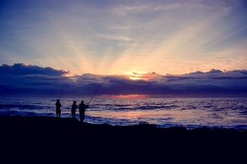 Fototapeta premium Men standing on the edge of rocks to catch fish from the ocean