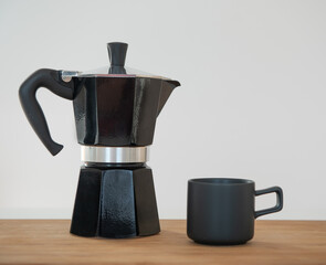 Cafetière italienne et tasse noir sur une table en bois devant un mur blanc avec de l'espace vide