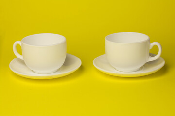 two white cups with a saucer on a yellow background