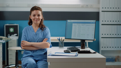 Portrait of woman working as medical assistant at desk in doctors office. Nurse looking at camera and smiling while preparing for work on computer. Healthcare specialist in uniform