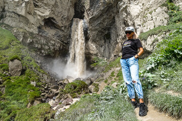 Naklejka na ściany i meble A girl at the Sultan-su waterfall surrounded by the Caucasus Mountains near Elbrus, Jily-su, Russia