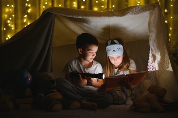 Obraz na płótnie Canvas happy family children reading a book with a flashlight in a tent at home