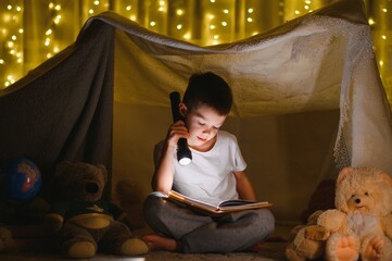 Preteen boy with flashlight reading book at home