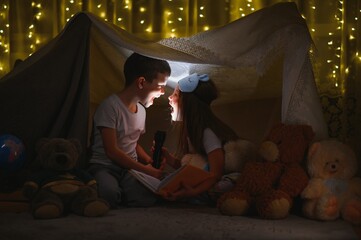 children boy and girl playing and frighten each other with flashlight in tent at night