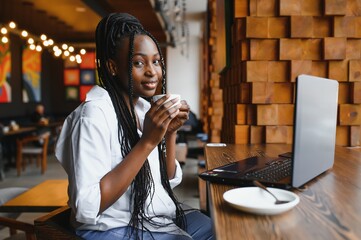 Young woman siting at cafe drinking coffee and working on laptop