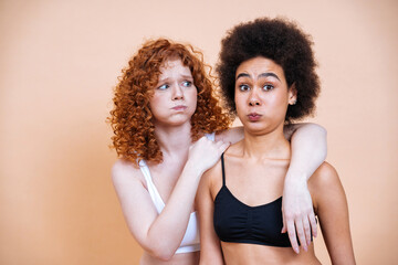 beauty image of two young women with different skin and body posing in studio for a body positive photoshooting. Mixed female models in lingerie on colored backgrounds