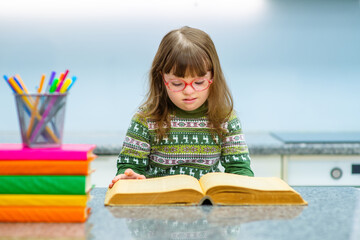 A child with down syndrome with glasses sitting at a table and reading a big serious book