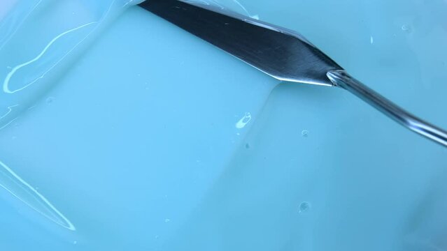 The texture of a blue cream or gel close-up. A metal spatula smears a blue substance on the surface. An advertising concept for face and body care cosmetics. Health care products.