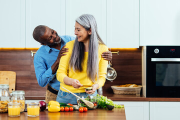 cinematic image of a multiethnic senior couple preparing food in the kitchen. Indoors Lifestyle moments at home. Concept about seniority and relationships