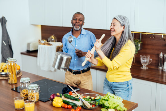 cinematic image of a multiethnic senior couple preparing food in the kitchen. Indoors Lifestyle moments at home. Concept about seniority and relationships