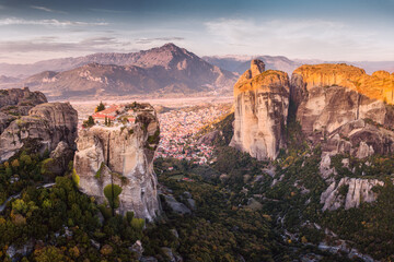Scenic panoramic view of the Monastery of the Holy Trinity in Meteora at sunrise and Kalambaka town at the distance. Tourist and pilgrimage experience. Natural and religious wonders of Greece.