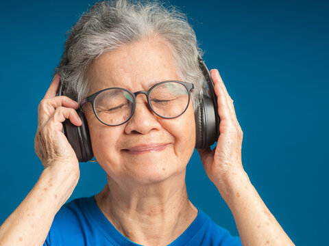 Senior woman wearing wireless headphones to listen to a favorite song and eyes closed with a smile while standing on a blue background
