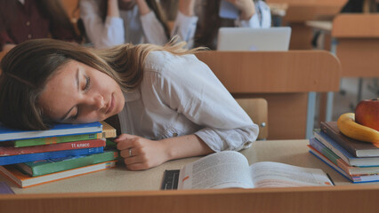 A tired schoolgirl falls asleep over her textbooks at her desk.