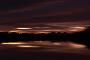 Rural landscape at twilight with fading light in long exposure - abstract dark cloud over mountain silhouette and reflection in river water