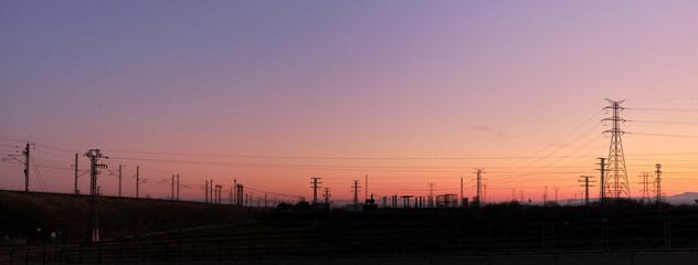 Obraz premium Panoramic sunset with the silhouettes of electric towers on the background