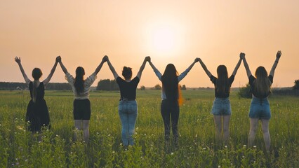 Girls friends raise their hands at sunset.