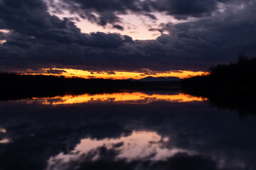 Naklejka premium Twilight landscape with dark ominous storm clouds and fading orange glow at sky above horizon - symmetric reflection