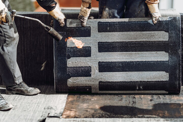 Construction workers, roofers installing rolls of bituminous waterproofing membrane for the...