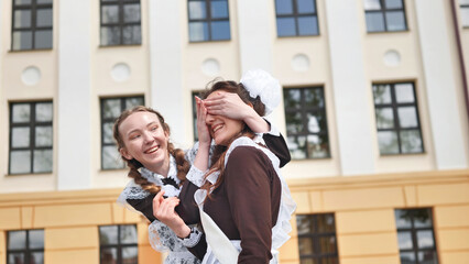 Happy schoolgirl graduate closes her friend's eyes.