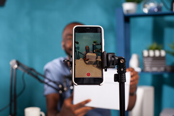 Closeup of live vlog setup with smarthone on stand filming smiling vlogger hosting online giveaway...