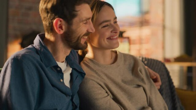 Close Up Portrait of Young Couple Spending Time at Home, Sitting on a Sofa, Man Embracing His Girlfriend While Watching Exciting TV Show in Apartment. Man and Woman Streaming Movie and Get Surprised.
