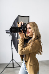 Young beautiful female posing for a photo shoot in a studio, a photographer is shooting with a digital camera - obrazy, fototapety, plakaty