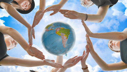 Schoolgirls hug the earth globe with their hands, making a circle out of them on the background of...