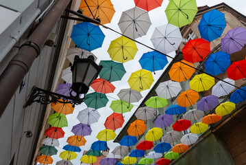Stara kuta latarnia uliczna na tle wielobarwnych parasolek rozwieszonych nad ulicą. Polska.