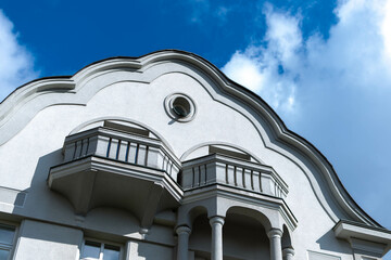 Fasada kamienicy z dwoma balkonami, delikatne zdobienia i lekko pochmurne niebo. Bielsko-Biała.