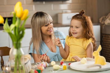 Obraz na płótnie Canvas Cheerful mother and daughter coloring eggs for Easter holidays