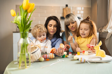 Obraz na płótnie Canvas Two women their little children decorate Easter eggs