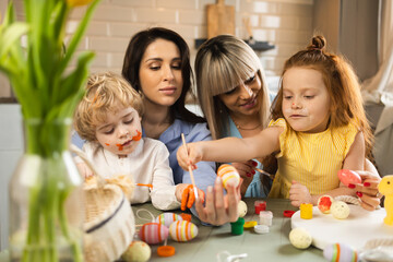 Happy mothers and their children decorating Easter eggs