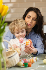 Mother and handsome little boy are preparing Easter decorations while sitting at the table in the kitchen