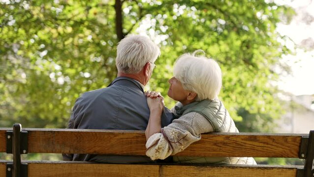 two elderly grey-haired caucasian people sitting on a bench in park and deepening their relationship. High quality 4k footage