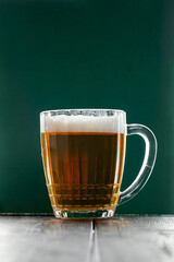 Mug with traditional Irish pale ale on dark green background. Bubbles in glass of beer.
