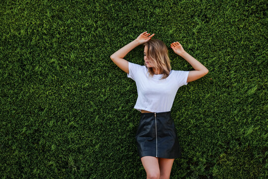 Young woman in white shirt and short black skirt standing by evergreen hedge