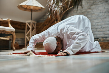 Religious Muslim man prostrating to God while praying at home.
