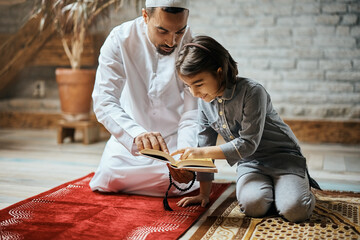 Religious Muslim father and daughter read from Koran while praying at home.