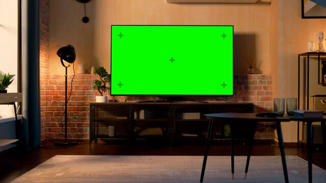 Stylish Loft Apartment Interior with TV Set with Green Screen Mock Up Display Standing on Television Stand. Empty Living Room at Home with Chroma Key Placeholder on Monitor. Zoom Out Sunset Warm Shot.