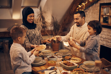 Happy Middle Eastern family shares pita bread at dining table on Ramadan. - obrazy, fototapety, plakaty