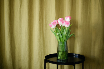 Bouquet of pink tulips on black table on a green linen background.