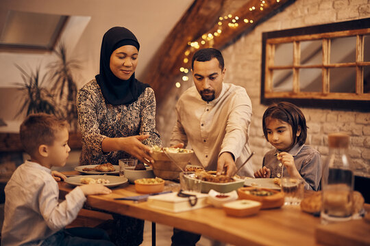 Traditional Muslim Parents And Their Kids Enjoy In Family Dinner At Dining Table.