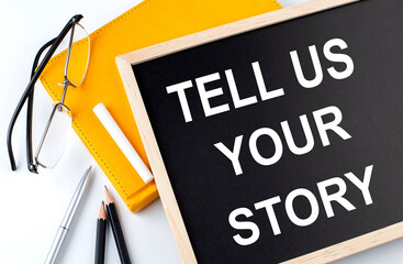 TELL US YOUR STORY text on the blackboard with notepad , pen, pencil