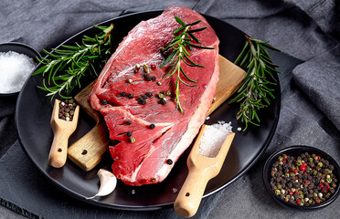 Steak meat with herbs and spices on wooden spoon on dark plate on the grey cooking apron
