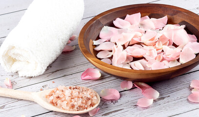 Rose petals on a wooden bowl with pink salt and white towel on wooden background