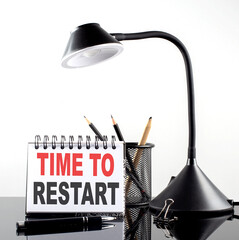TIME TO RESTART text on notebook with pen and table lamp on the black background