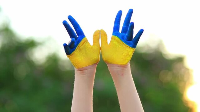 Child hands painted in Ukrainian flag colors waving hello outdoor on nature background. Ukraine Independence Day, 24 August