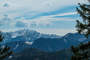 Scenic view of snow capped mountain peaks of Karawanks on the way to Sinacher Gupf in Carinthia, Austria. Mount Wertatscha is visible through dense forest in early spring. Rosental on a sunny day.Hike