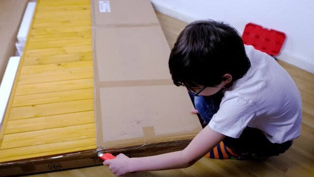 child 9-10 years assemble wooden furniture from parts together at home, boy unpacks parcel with utility knife, concept to convey experience, order furniture by mail, happy family